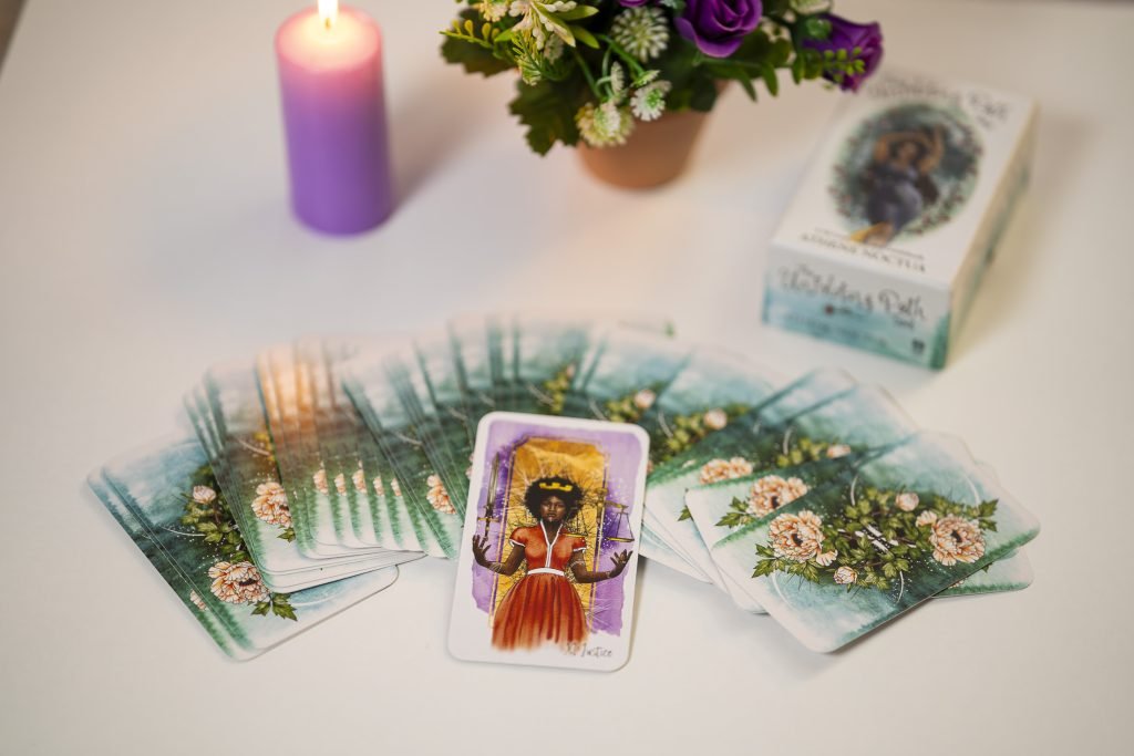 Cartas de tarot extendidas con una carta central, vela violeta y flores, lectura Retos y Aprendizaje