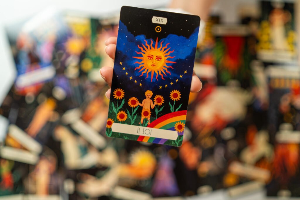 Carta de tarot El Sol sostenida con la mano, sobre un fondo de cartas difuminadas, lectura Amor Propio