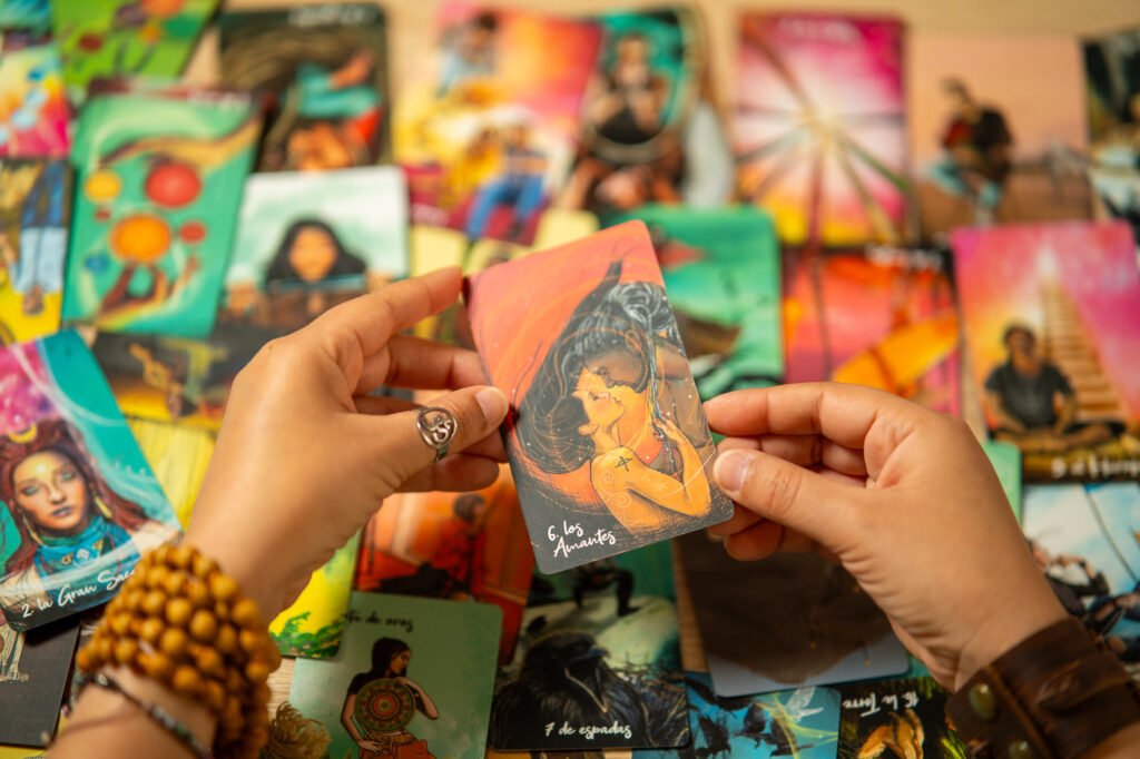Manos sosteniendo la carta de tarot ‘Los Amantes’, rodeada de un despliegue colorido de barajas, en la lectura ‘Desbloquea Tu Potencial’
